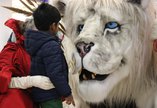 An adult and a child are looking at a large snow lion puppet