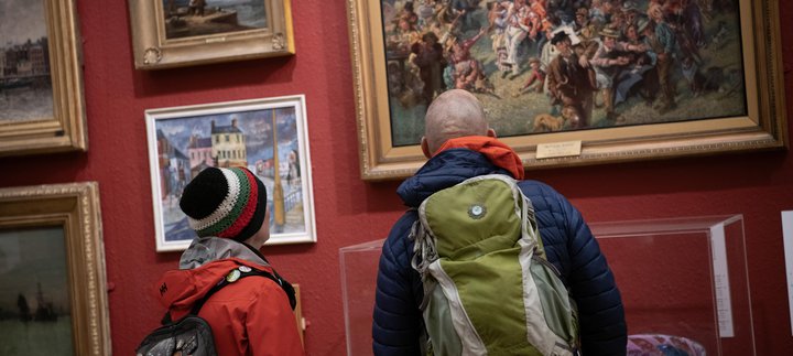 Two visitors standing and looking at a painting on a red gallery wall.