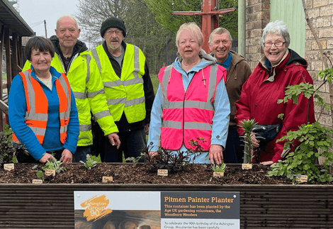 A group of men and women volunteers stand in front of a planter at Woodhorn Museum