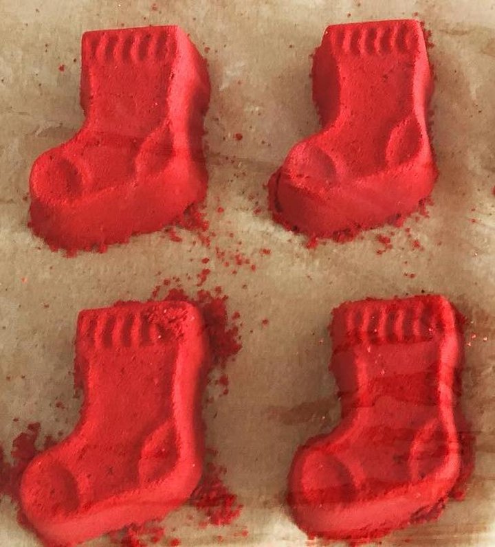 A photograph of four red bath bombs in the shape of Christmas stockings.