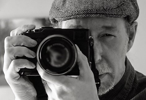 A close up portrait of a man wearing a hat and holding a camera up to his face