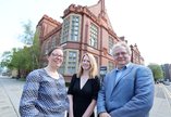 A group of three people standing in front of a historic red brick building. 