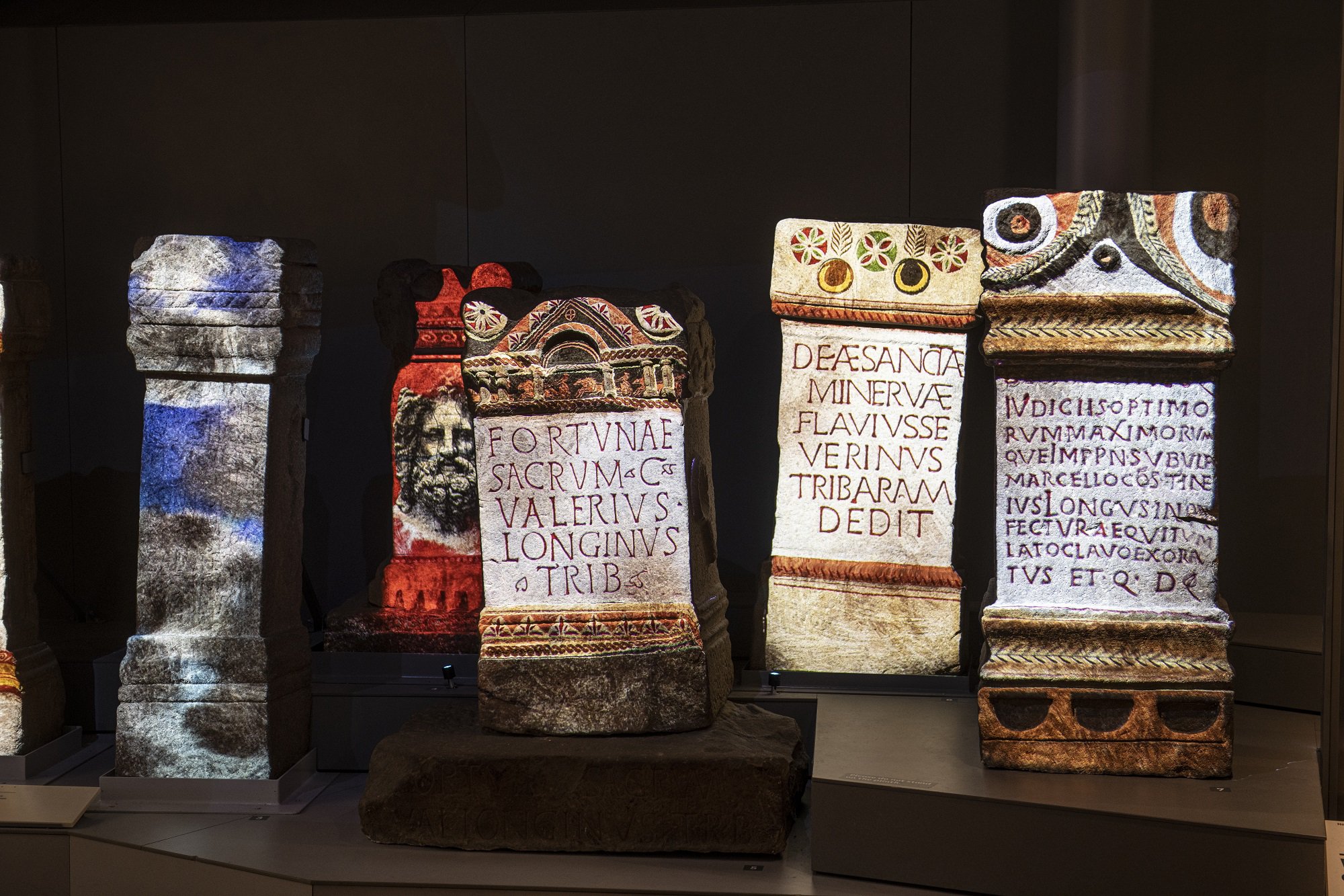Five Roman stone altars with colourful animations projected onto them.
