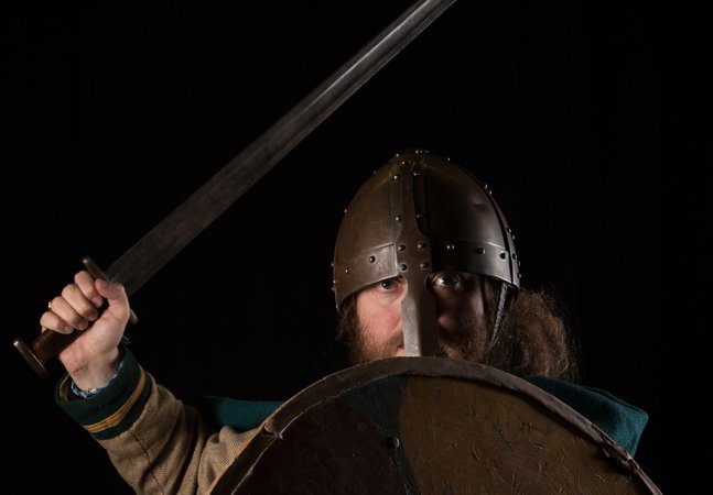 A man wears a viking helmet and holds a shield and sword.