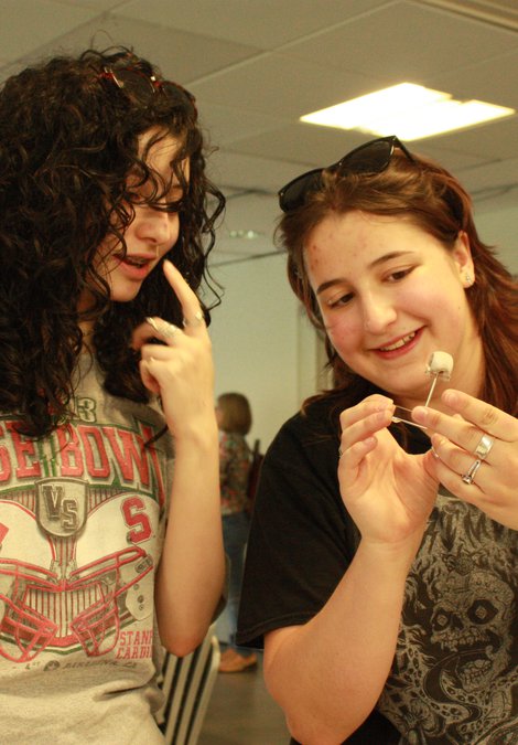 2 young women, one of the left looking at an object the woman on the right is holding (a mounted bird skull model)
