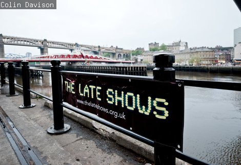 The Late Shows yellow and black banner on Gateshead quay with Swing and High Level bridges in the distance