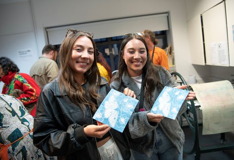 Two females in an artist studio smiling and displaying their prints