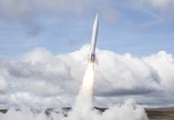  Launch of white rocket on moorland with blue sky and fluffy white clouds behind