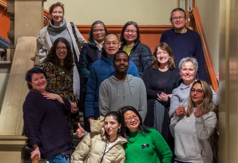 A group photograph of 13 individuals on a staircase in an art gallery.