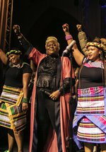 A group of people stand on a stage, they are smiling and each person has one arm raised in the air.