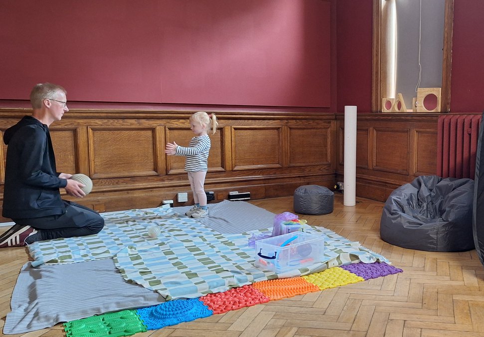 An adult and child throwing a ball to each other in a play space.