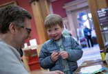 An adult and child laughing and smiling at a craft event inside an art gallery