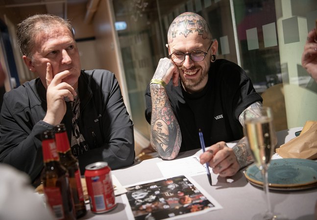 two men sit a table playing a quiz, laughing