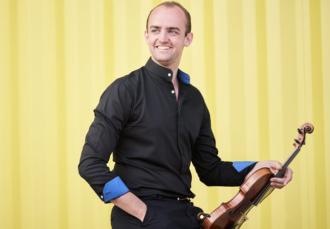 A man in a black button down shirt holding a violin