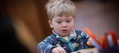 A child with short blonde hair sitting at a table and taking part in a craft activity