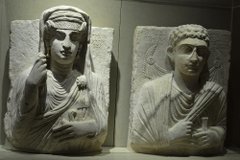 Two finely carved stone artefacts showing human figures. They are both shown wearing draped fabrics