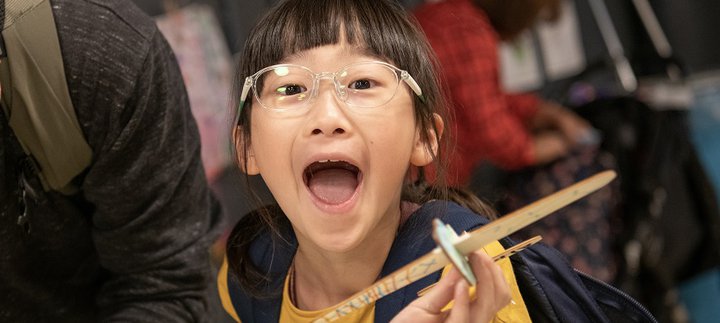 girl in Play Invent gallery holds her creation and laughs at camera