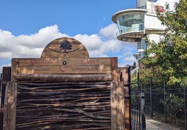 Wooden sign marking end of Hadrian's Wall trail with viewing tower in the background