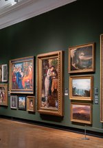 A photograph of the inside of the gallery. Oil paintings in frames hang on a green wall.