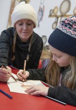 Woman and young girl wearing woolly hats sitting at a table doing a craft activity