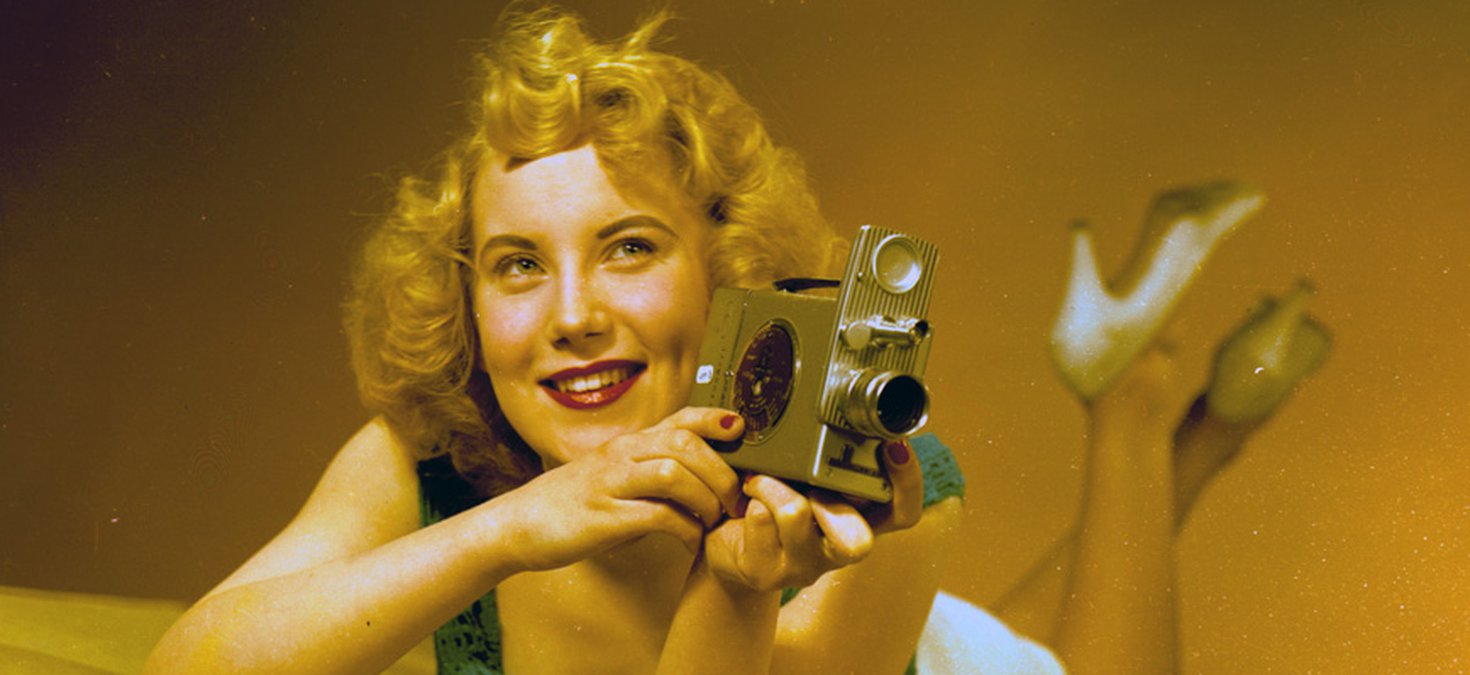 View of the model, Irene Warren, posing with a film camera for a Turners publicity shot, January 1957