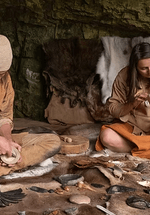 Two people are sat on the ground doing ancient crafts  