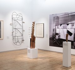 Several artworks are on display, a brass sculpture is the foreground of the photo, the shape of the sculpture resembles paper and corrugated cardboard that has been cut and stacked in various ways.