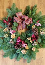 A photograph of a Christmas wreath decorated with dried oranges, pinecones, ribbons, and other decorations.