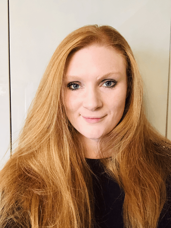 A person with long red hair and a black top, looking at the camera. A person with long red hair and a black top, looking at the camera.