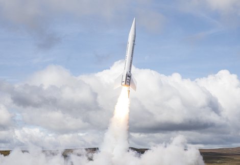 Launch of white rocket on moorland with blue sky and fluffy white clouds behind