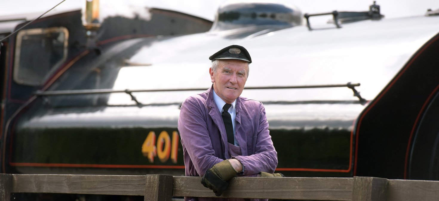 Man with cap in front of black steam locomotive