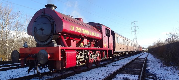Red steam locomotive pulling passenger carriages on snow covered railway