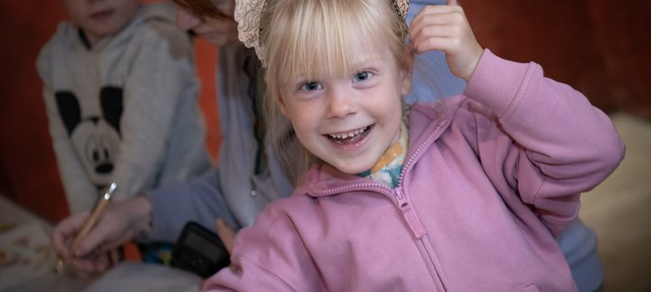 A child is wearing a paper helmet and smiling at the camera