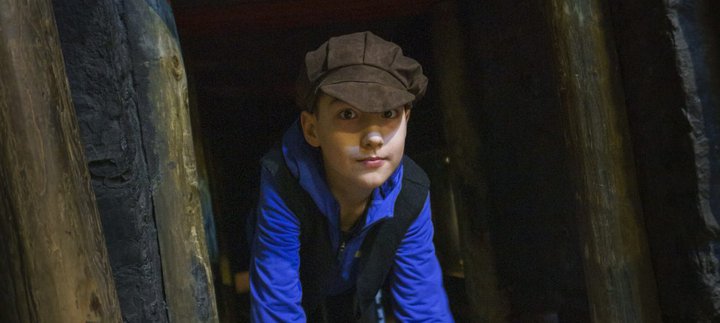 A child crawls through a museum display of a coal mine wearing a flat cap