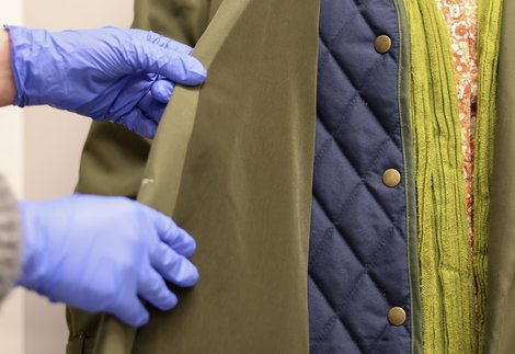 a blue gloved hand holds the lapel of a heavy coat
