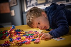 A child leans over a table and plays with a set of colourful  atom shaped toys