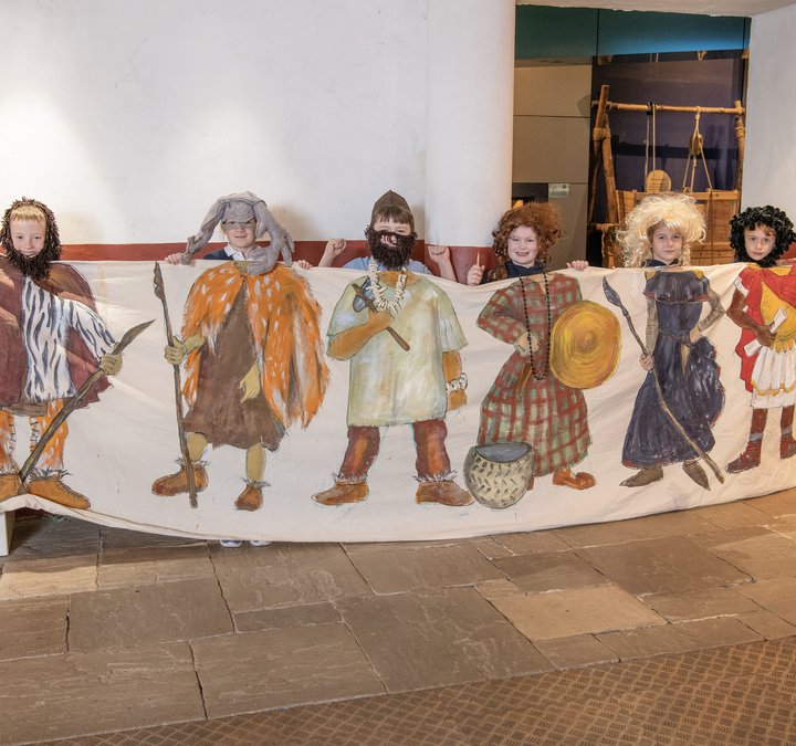 Line of school children behind a long piece of cloth with pictures of people in clothing from different time periods