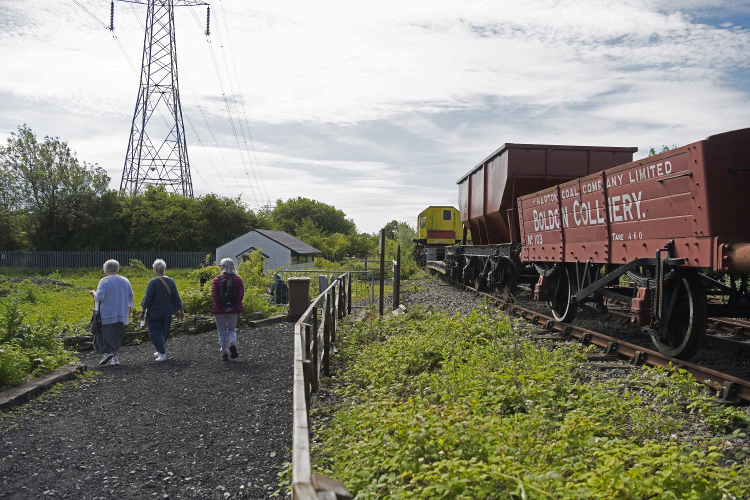 Three people walk alongside a railway track with a freight carriage on the line Three people walk alongside a railway track with a freight carriage on the line